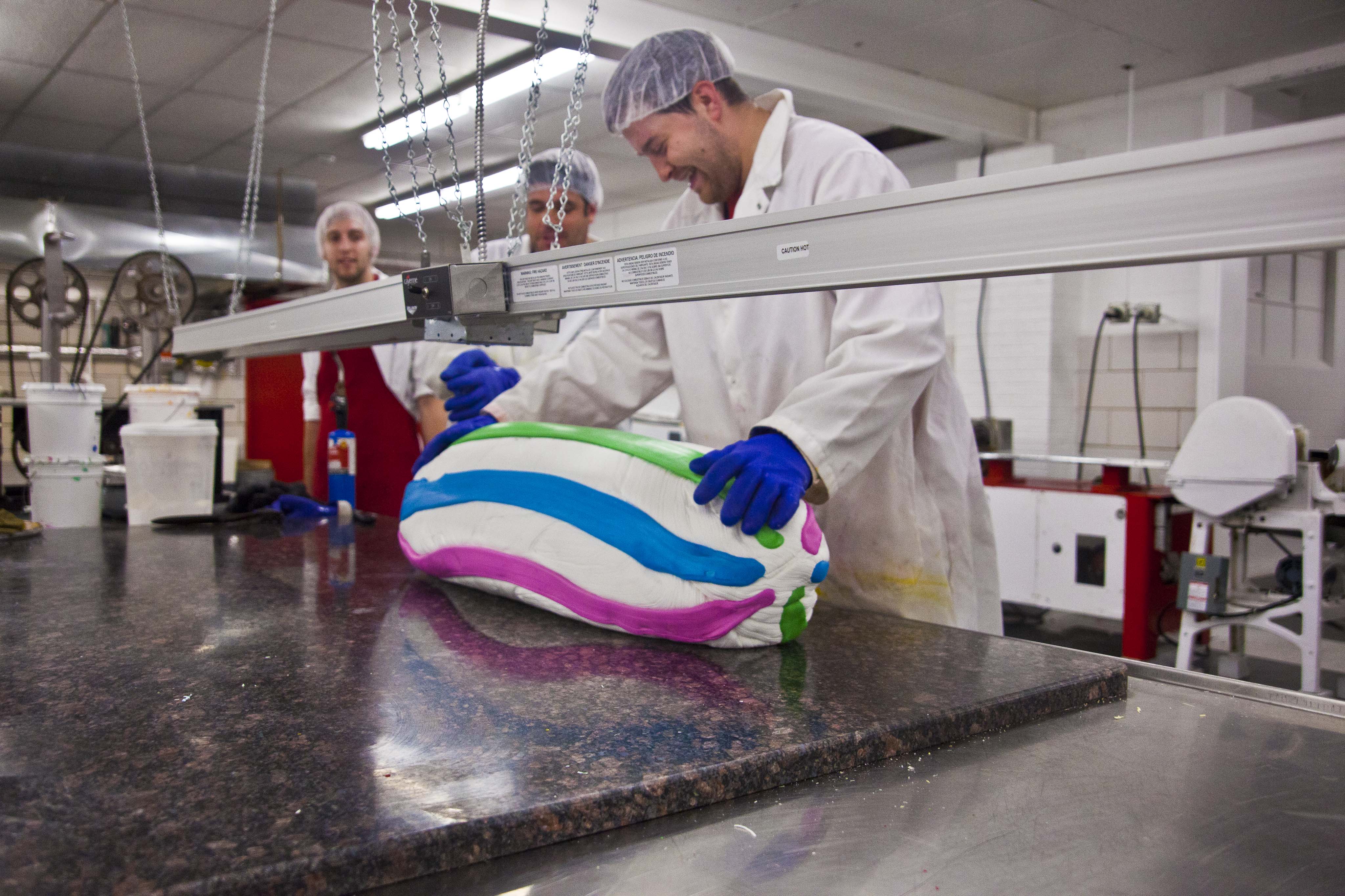 Dauphin and Shawn Freeder supervise Paul Freeder adding stripes to a custom mint batch. At size, the stripes will appear evenly on the top and bottom of the candies.