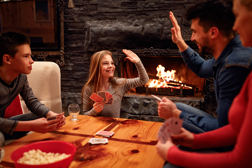 Family playing cards together around fireplace