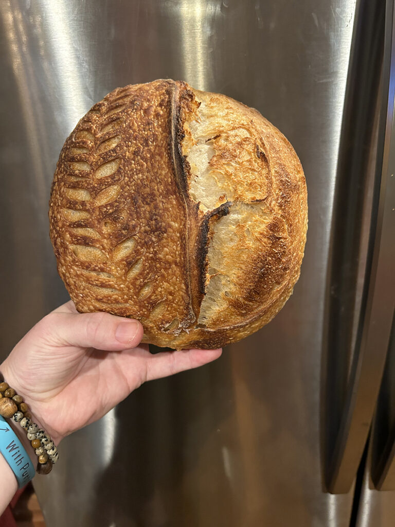 holding round loaf of sourdough bread
