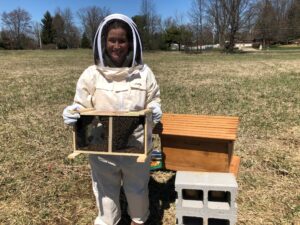 Sarah in beekeeping gear with hive